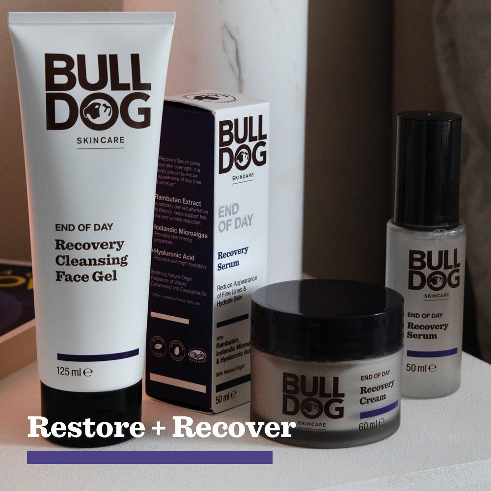 A Bulldog Skincare set with a cleansing face gel, End of Day Recovery Serum with hyaluronic acid, recovery cream, and box is arranged on a white surface, with Restore + Recover displayed below the products.