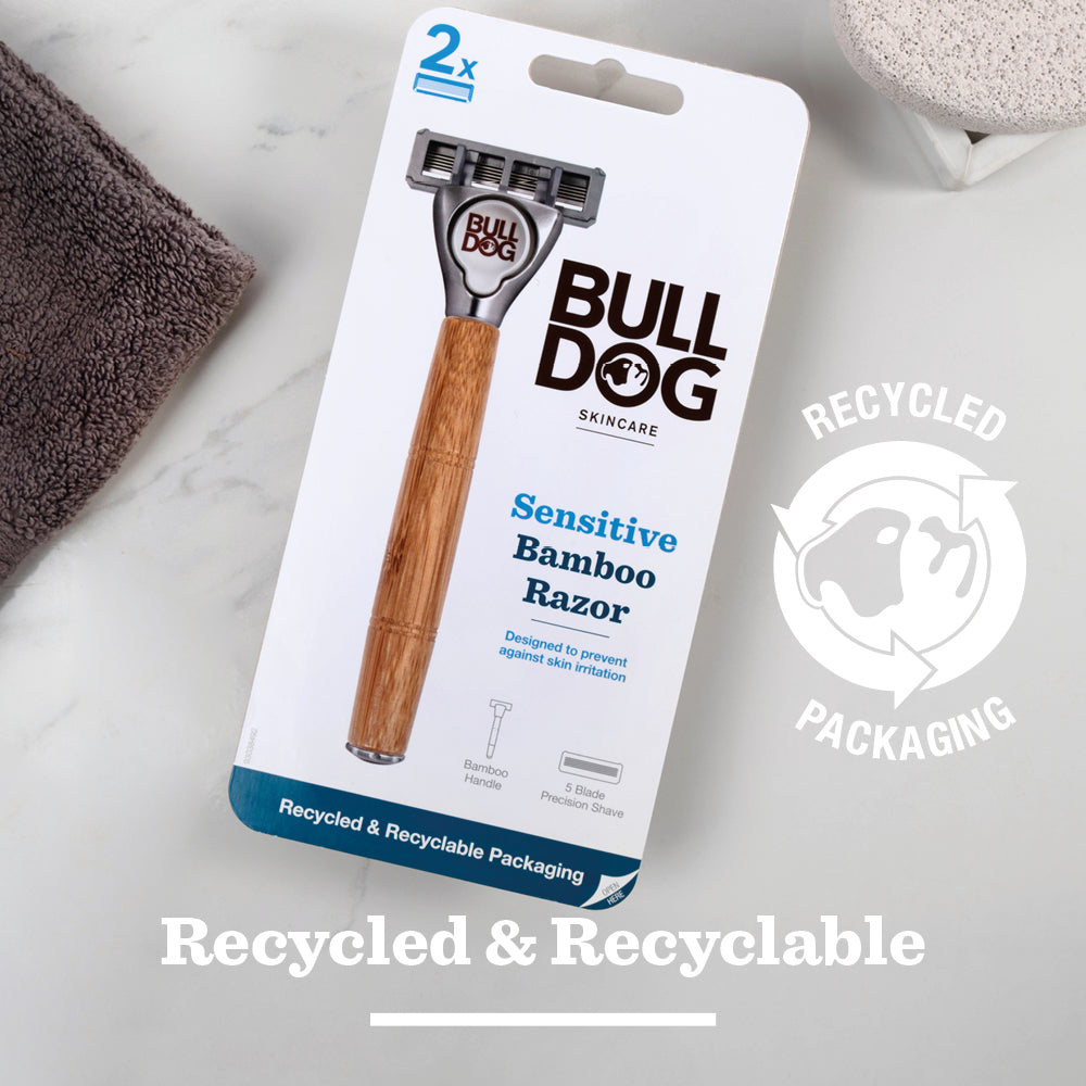 The Sensitive Bamboo Razor is shown on a marble surface beside a gray towel. Its recycled and recyclable packaging highlights an eco-friendly choice for a gentle shave with its bamboo handle and sensitive steel blades.