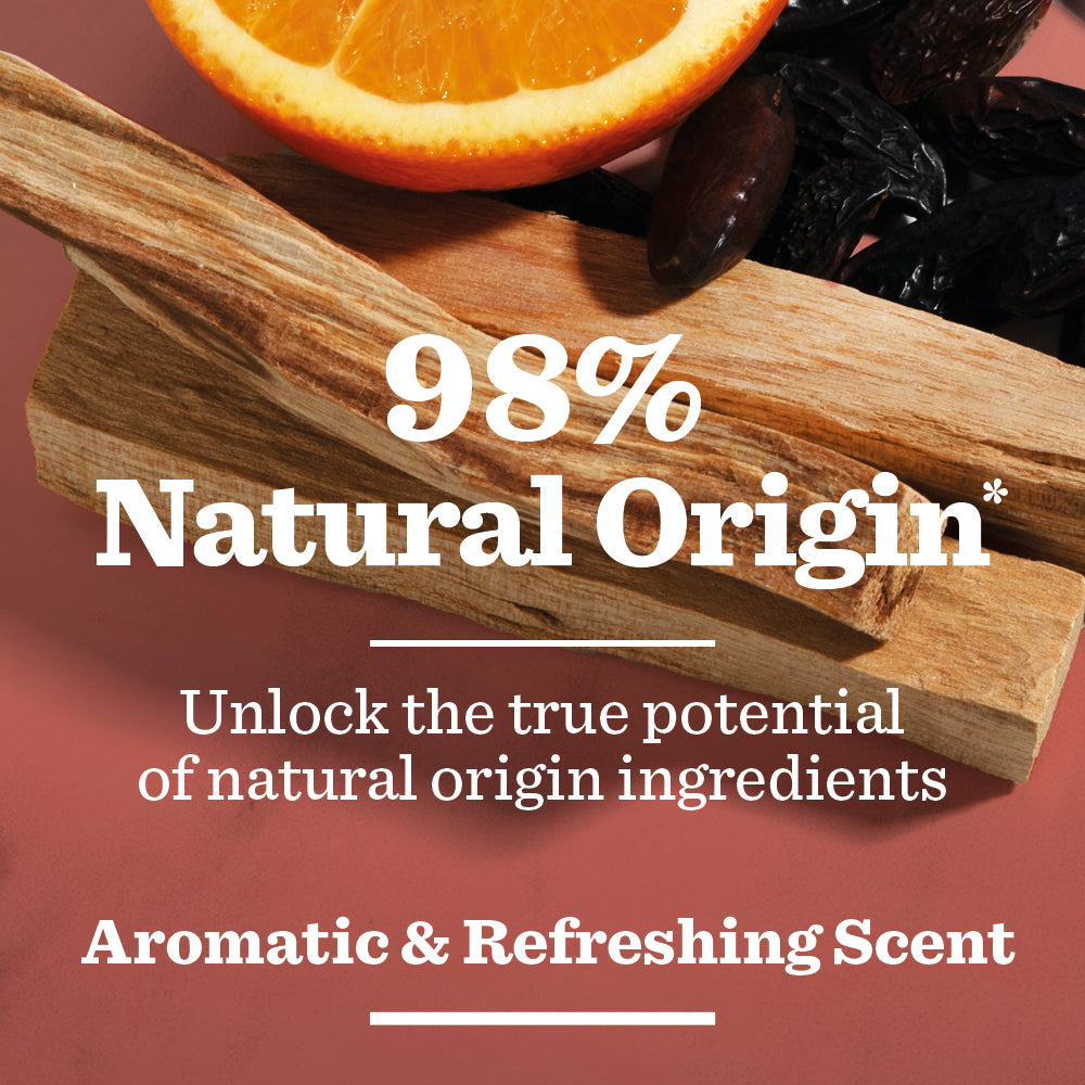 A slice of orange, a wooden stick, and dark seeds on a pink surface with the text: 98% Natural Origin*. Unlock the true power of natural origin ingredients with Bergamot in the Energising Spray Deodorant Bundle for an aromatic & refreshing scent.