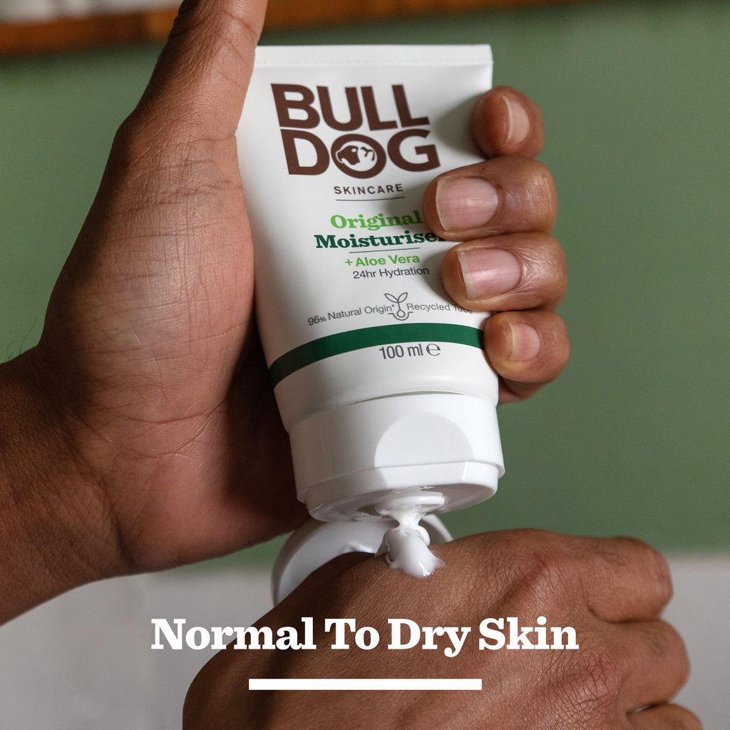 A hand squeezes a tube from the Premium Gift: Shave Collection, dispensing cream. Text below reads Normal To Dry Skin. The soft green background makes it an ideal gift for men who appreciate quality skincare.