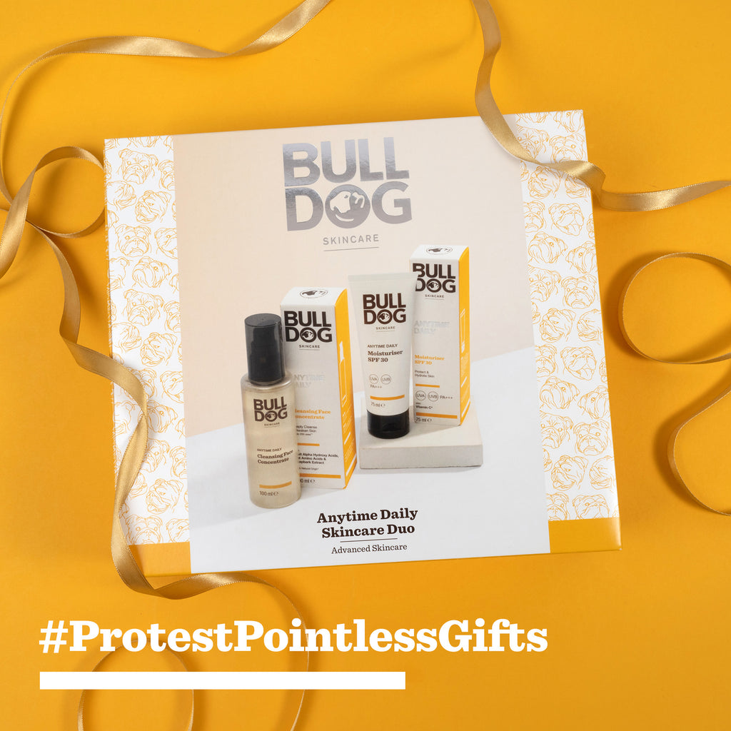 The Advanced Anytime Daily Duo gift set, made with natural origin ingredients, is shown on a white and gold patterned background with curled gold ribbon. Bold yellow text reads “#ProtestPointlessGifts.”.