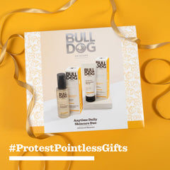 The Advanced Anytime Daily Duo gift set, made with natural origin ingredients, is shown on a white and gold patterned background with curled gold ribbon. Bold yellow text reads “#ProtestPointlessGifts.”.